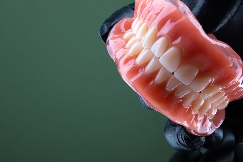 a full set of dentures with a dentist wearing a glove holding them up at an angle